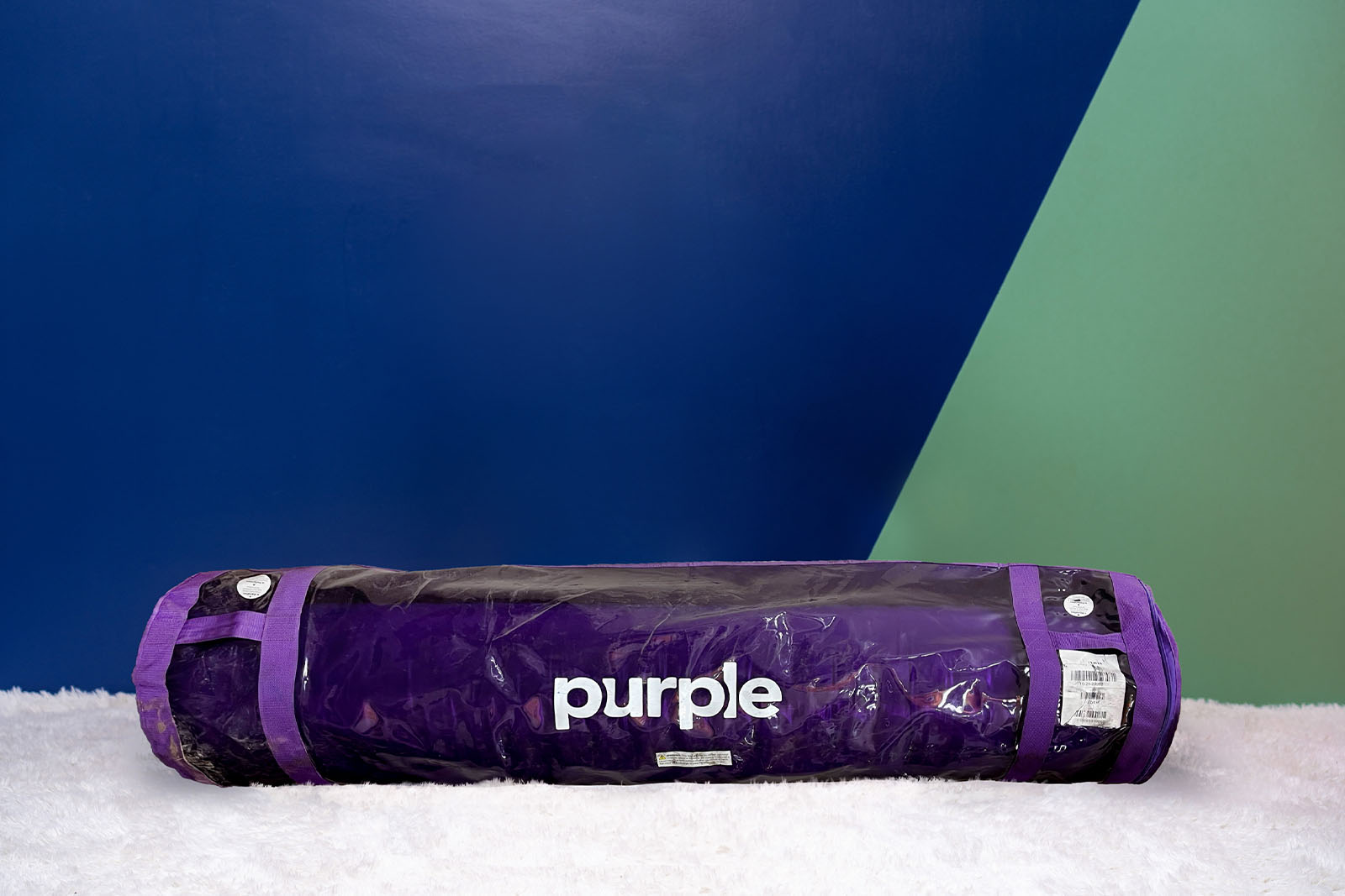 Photo of the Purple Restore Hybrid Mattress bag on the floor in a bedroom taken from a front angle.